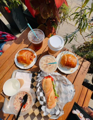 Fresh croissants, a gourmet sandwich, and coffee on an outdoor café table surrounded by greenery in the Shenandoah Valley.