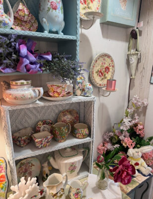 Floral teacups, plates, and vintage-style decor arranged on pastel shelving.
